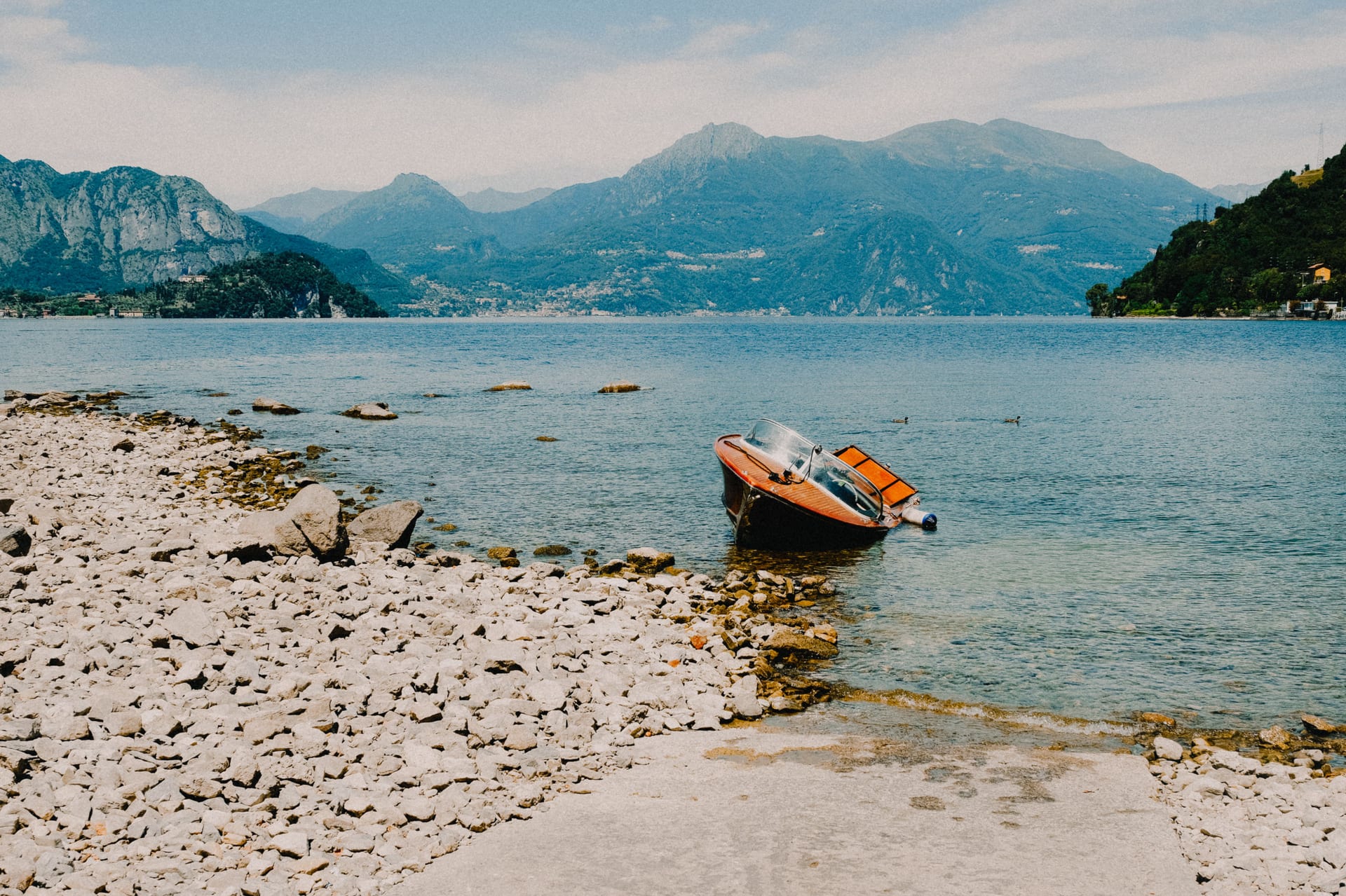 Une rive de galets et de pierres sur le lac, avec un bateau en bois et les montagnes en arrière-plan