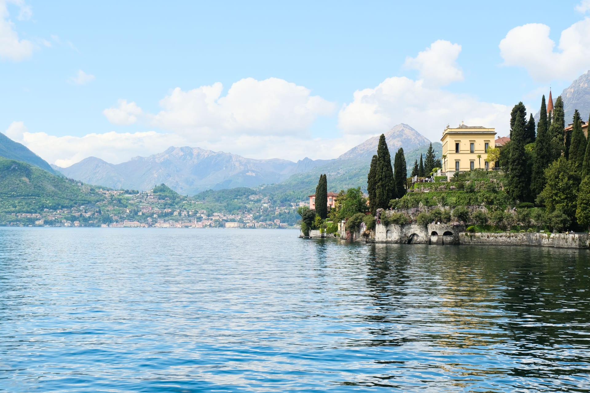 Eine Villa mit Zypressengarten auf einer Landzunge bei Varenna, im Hintergrund die Berge des Comer Sees