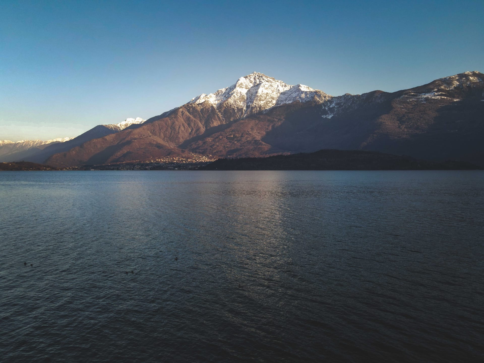 Der schneebedeckte Monte Legnone spiegelt sich im Wasser des Comer Sees unter klarem Himmel