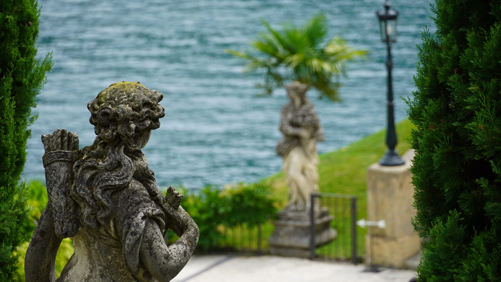 Stone statues in a historic villa garden, with the lake behind them