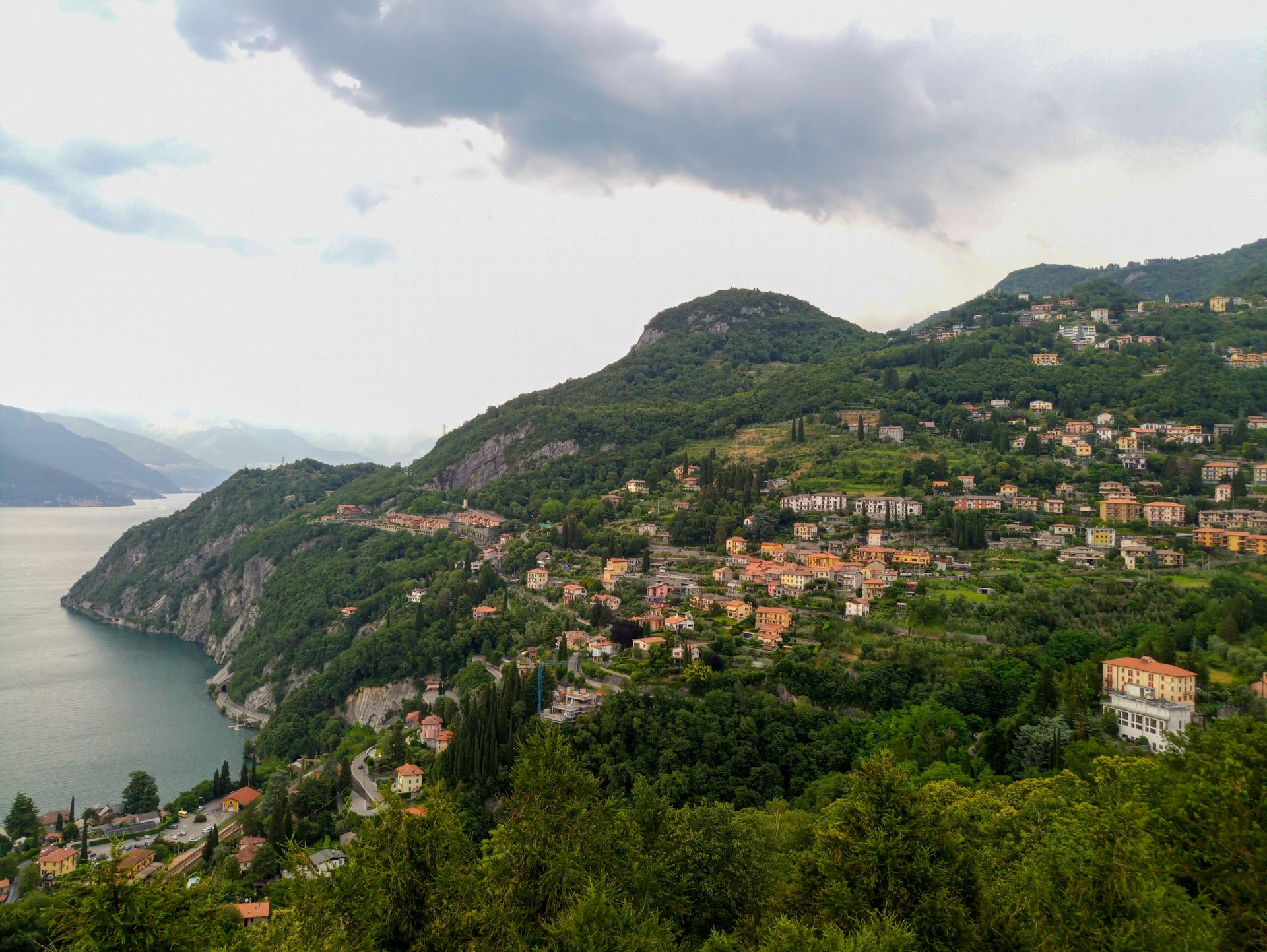 Villages on a green hillside above Lake Como, seen from above under a cloudy sky