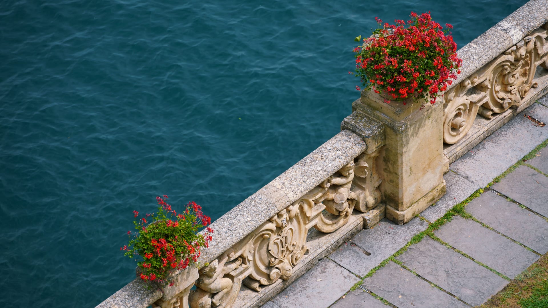 Steinerne Balustrade mit Töpfen roter Geranien über dem stillen Wasser des Comer Sees