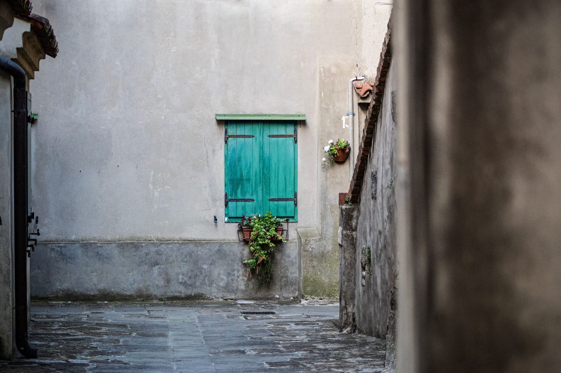 Un angolo di borgo con muri in pietra, una persiana verde e vasi di fiori