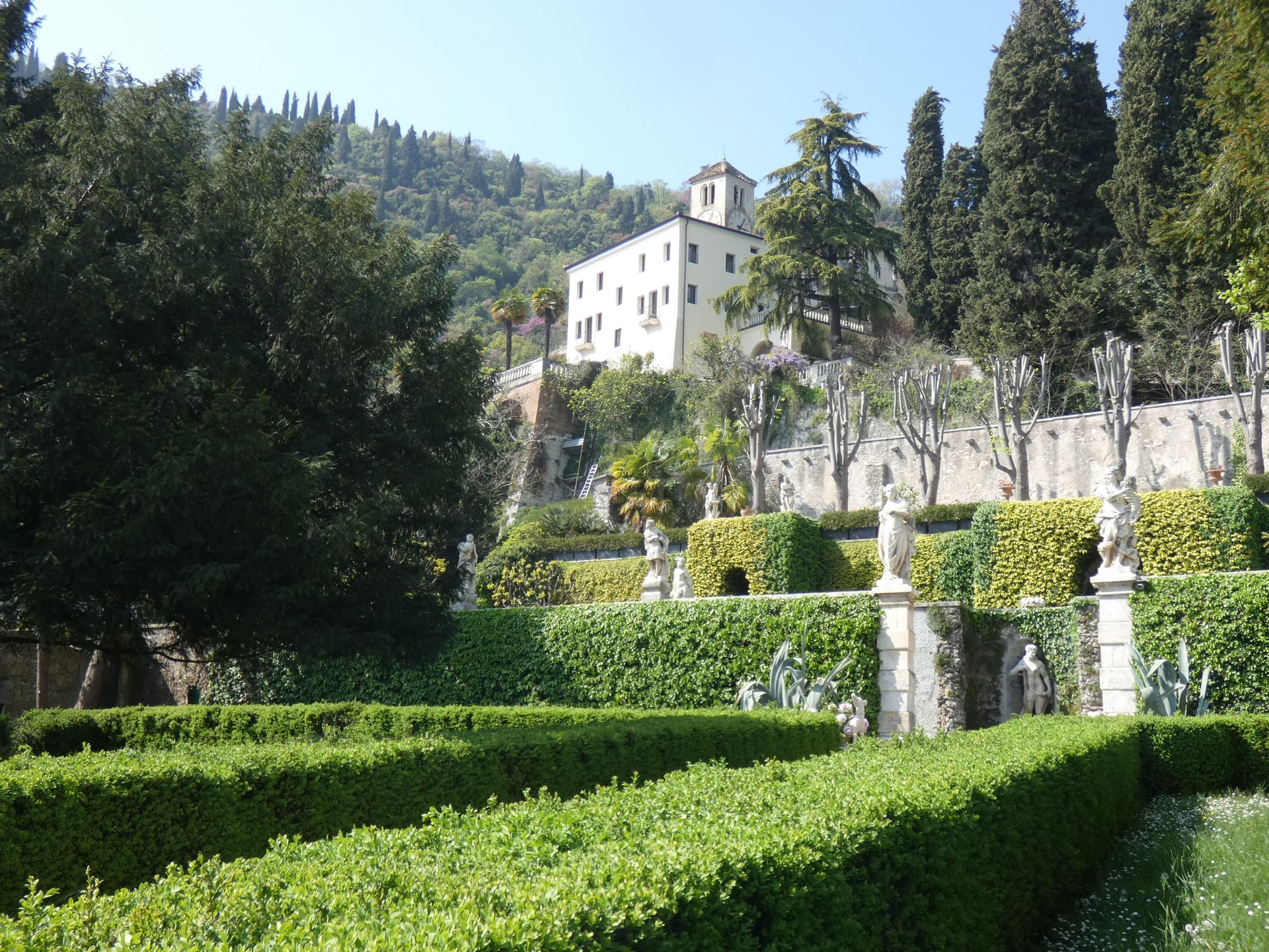 Il giardino di una villa storica italiana, con siepi potate e statue lungo il vialetto