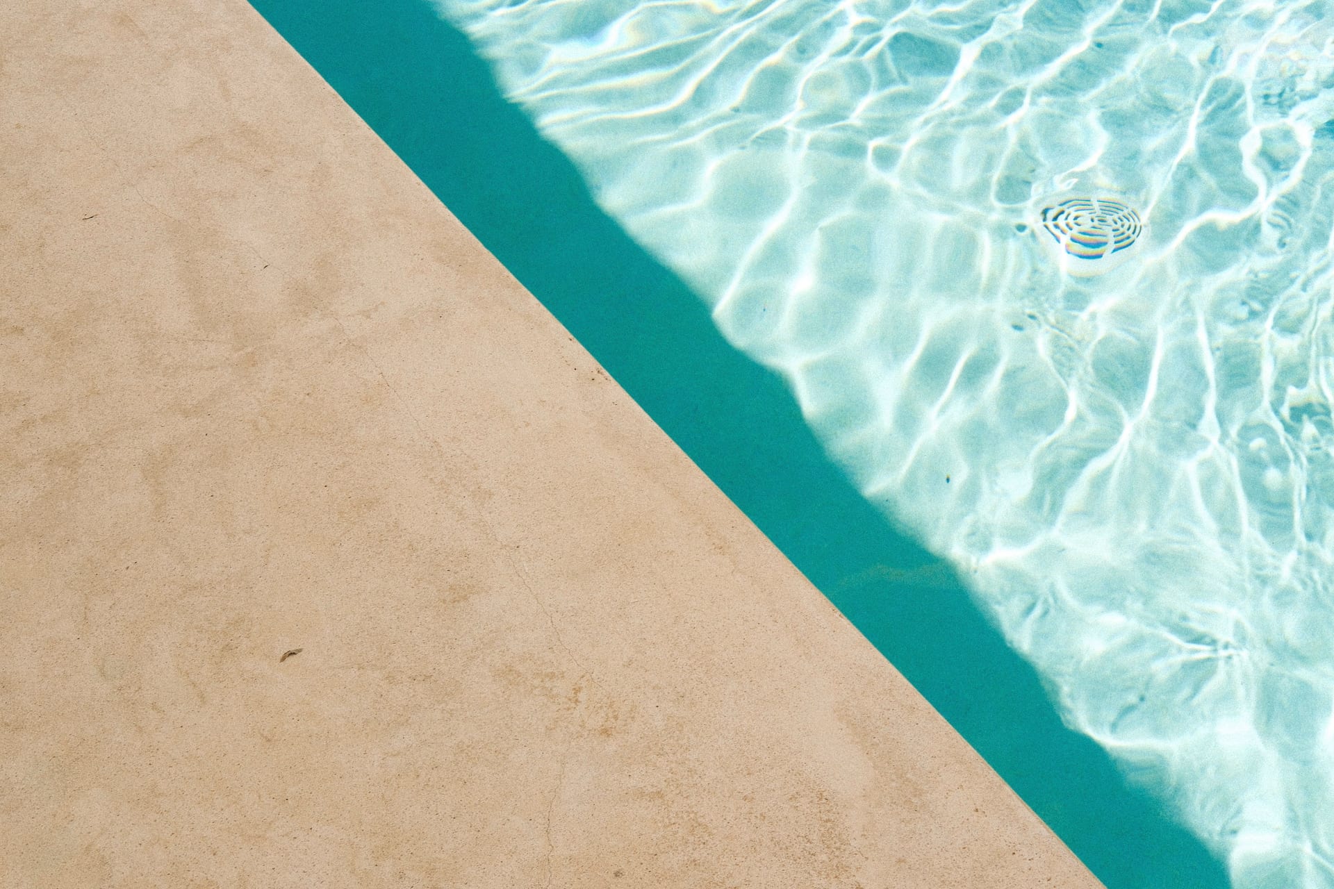 Der helle Steinrand eines Pools und türkisfarbenes, von der Sonne gekräuseltes Wasser